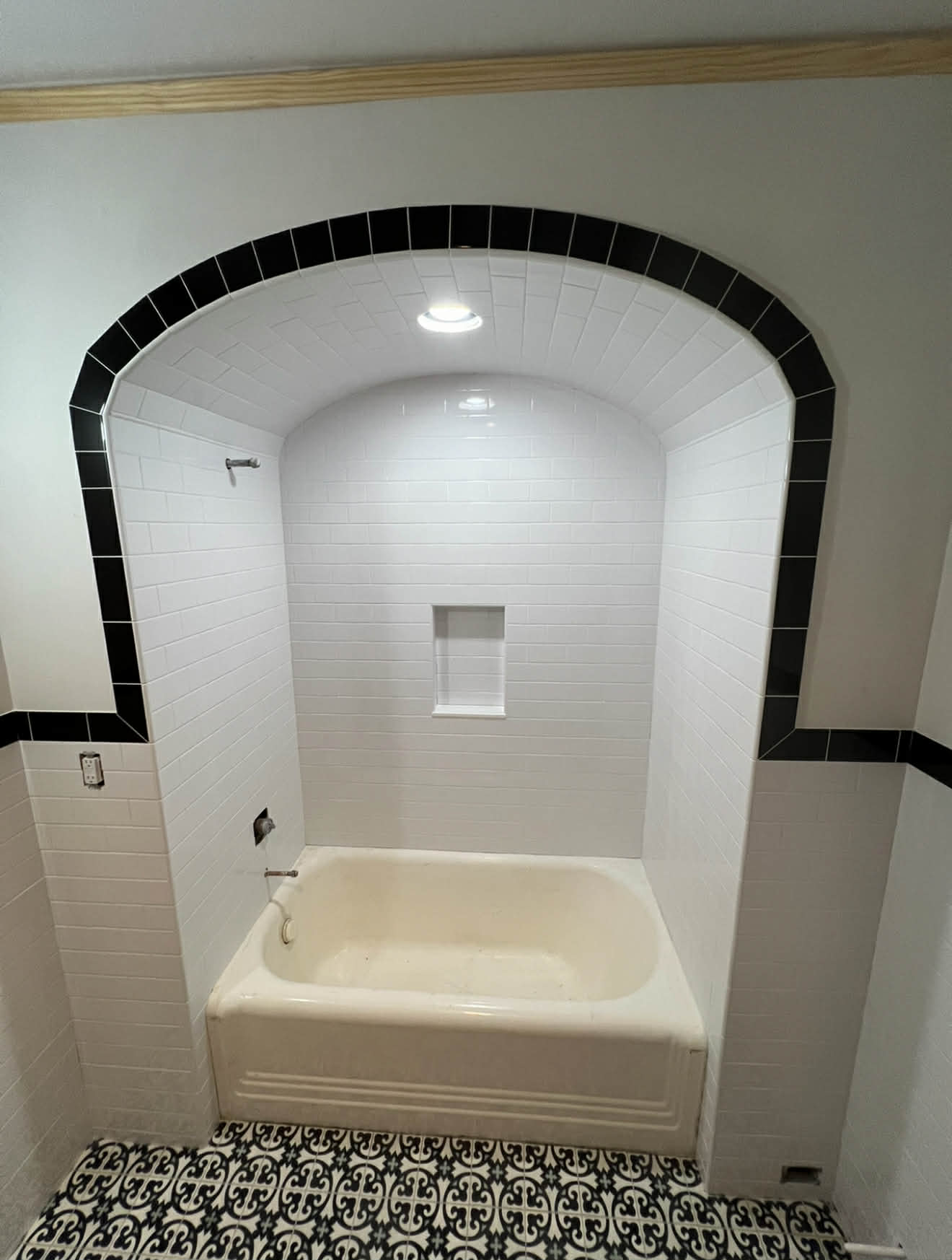 Bathtub in arched alcove with black border and patterned floor